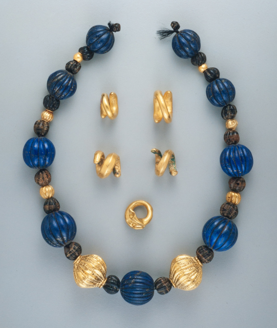 The necklace in this set has beads of gold, lapis lazuli, and hematite. The largest beads are spherical and ribbed like melons: nine of them are made of lapis lazuli and two are gold. Five spiral rings of gold are also included in this group.