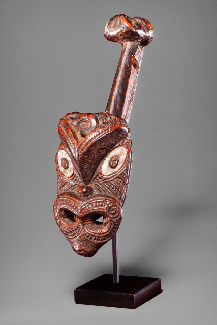 A unknown object with two heads, one large and one small, at the two ends of a wooden pole. The eyes are inlaid with shell.