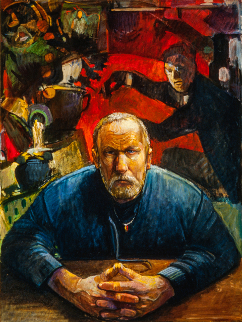 Portrait of a man with white hair and a blue shirt leaning forward on a table with hands clasped together. Behind him is a painting with a figure and geometric shapes.