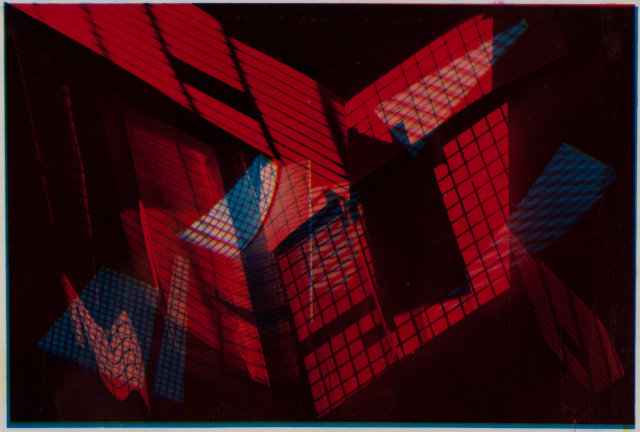 A horizontal color photograph depicts intersecting patterns of grids and screens. The dominant colors are red, blue, and brownish tones.